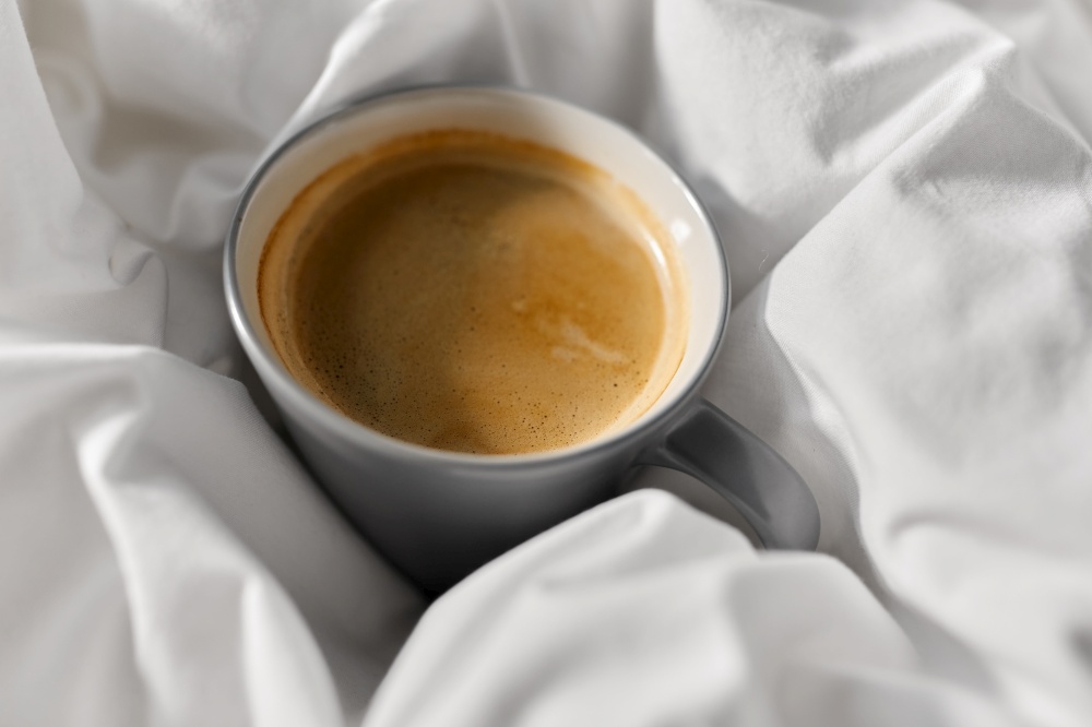 morning, hygge and drink concept - cup of coffee in bed at home. cup of coffee in bed