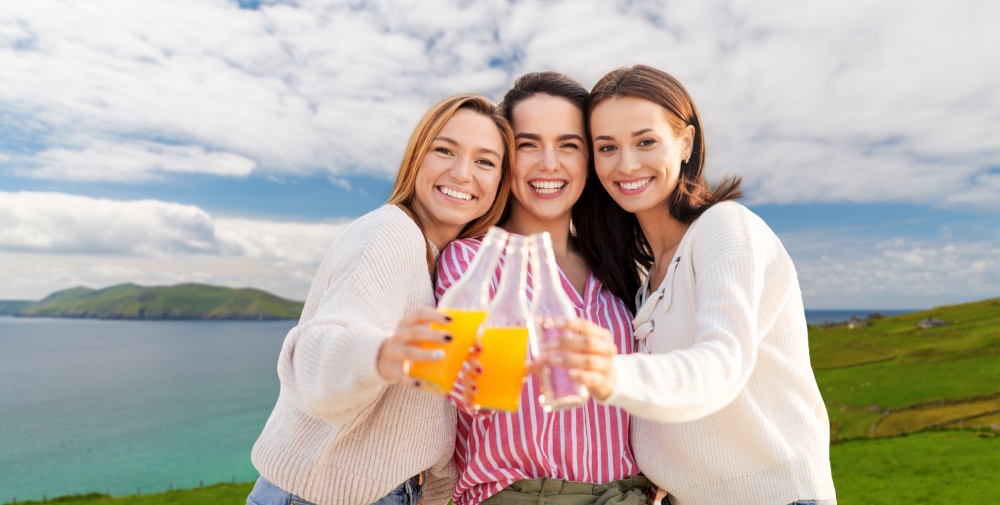 travel, tourism and friendship concept - group of happy young women or female friends toasting non alcoholic drinks over ireland on background. women toasting non alcoholic drinks in ireland