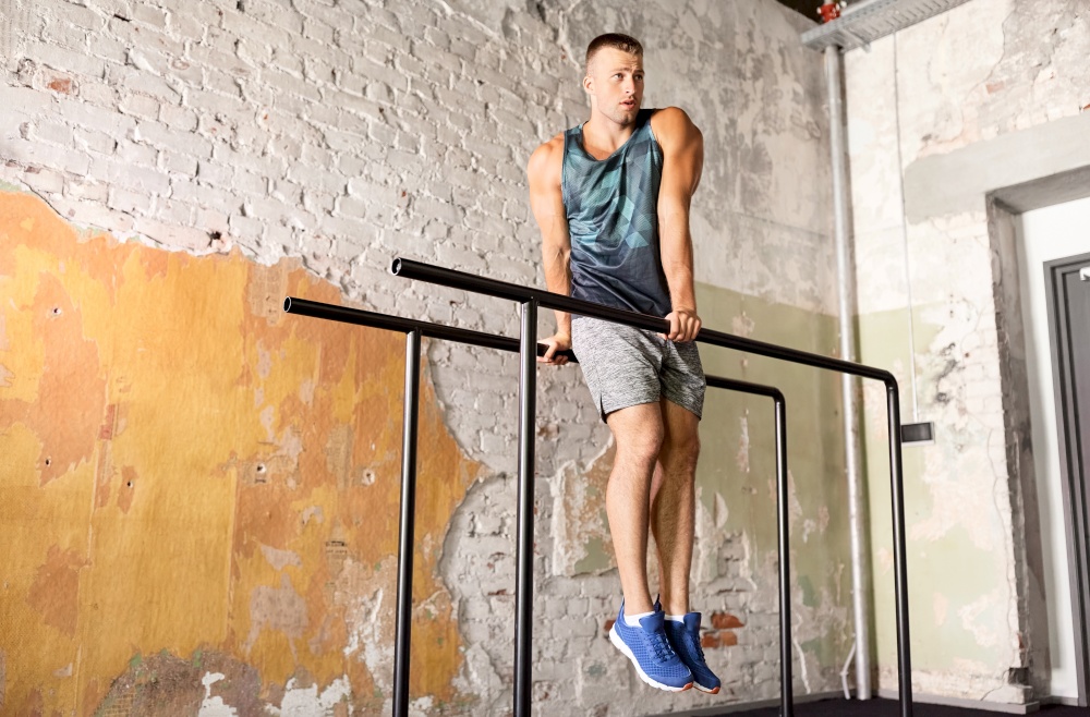fitness, sport, bodybuilding and people concept - young man doing abdominal exercise on parallel bars in gym. man flexing abs on parallel bars in gym