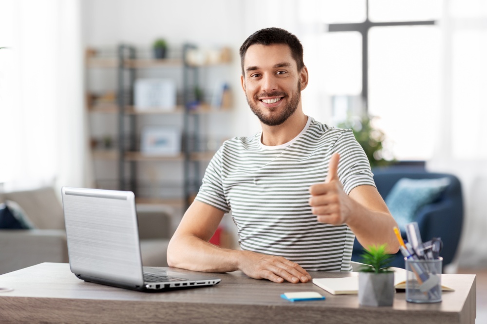 technology, remote job and business concept - happy smiling man with laptop computer showing thumbs up at home office. happy man with laptop working at home office