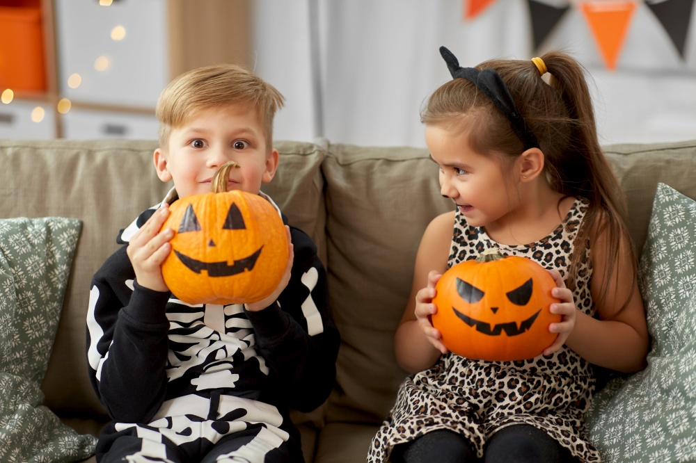 halloween, holiday and childhood concept - smiling little boy and girl in costumes with jack-o-lantern pumpkins having fun at home. kids in halloween costumes with pumpkins at home