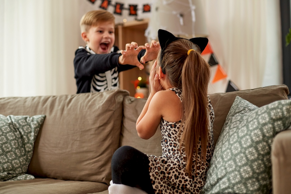 halloween, holiday and childhood concept - smiling little boy and girl in costumes having fun at home. kids in halloween costumes having fun at home
