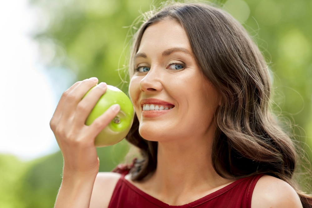 healthy eating, dental and people concept - portrait of happy woman with green apple at summer park. happy woman eating green apple at summer park