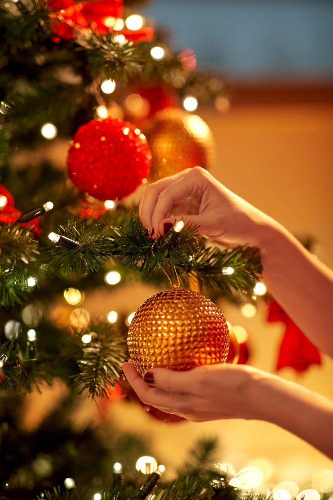 holidays, celebration and people concept - woman hands decorating christmas tree with ball. hands decorating christmas tree with ball