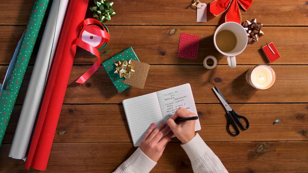 holidays, new year and christmas concept - female&rsquo;s hands writing to do list in notebook on wooden table. hands writing to do list in notebook on christmas