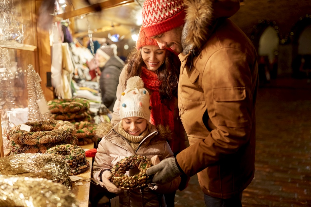 family, winter holidays and celebration concept - happy mother, father and little daughter buing wreath at christmas market on town hall square in tallinn, estonia. happy family buing wreath at christmas market