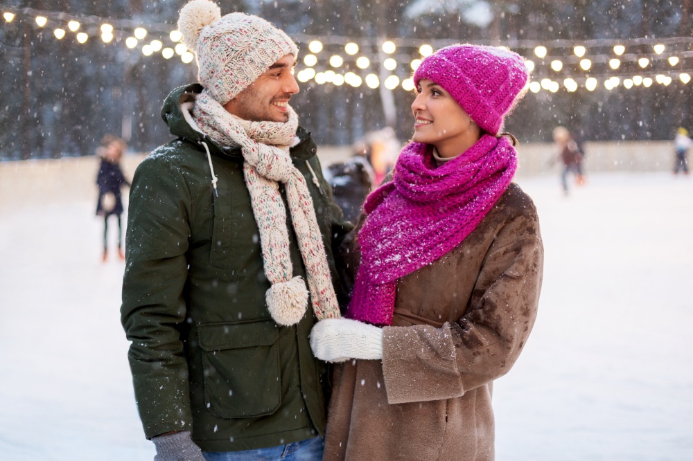 people and leisure concept - happy smiling couple talking at outdoor skating rink in winter. happy couple at outdoor skating rink in winter