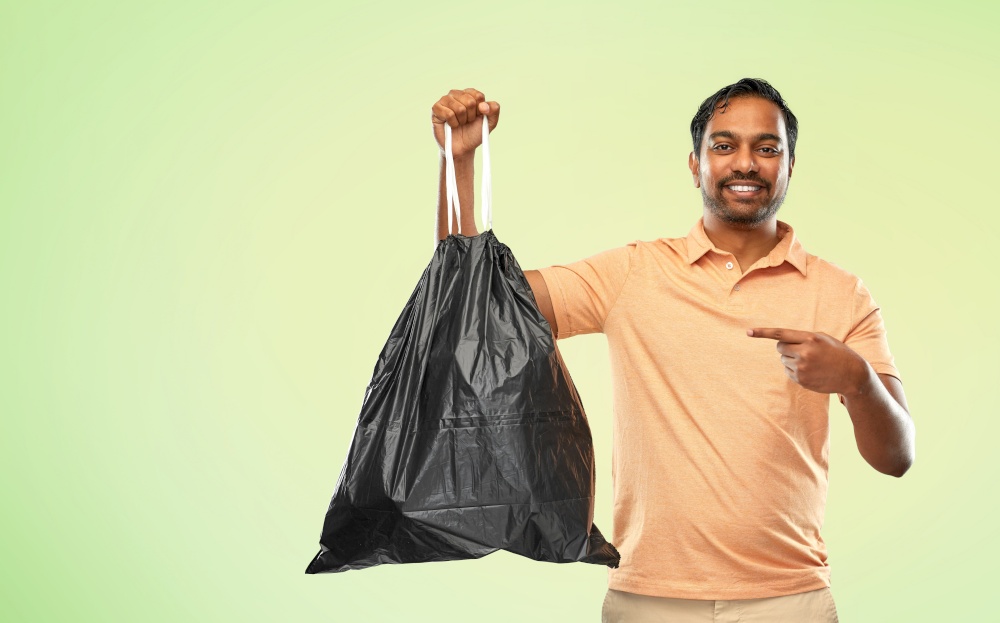 recycling, sorting and sustainability concept - smiling young indian man holding trash bag over green background. smiling indian man holding trash bag