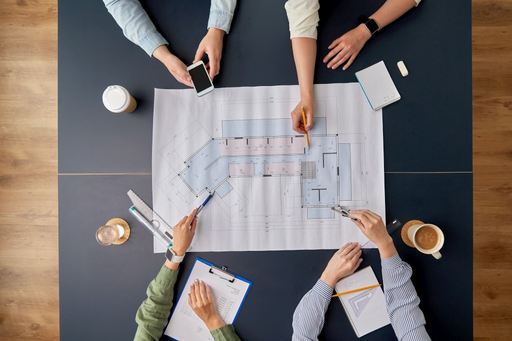 construction business, architecture and team work concept - team of architects with blueprint, gadgets and papers working at office table. business team with blueprint working at office
