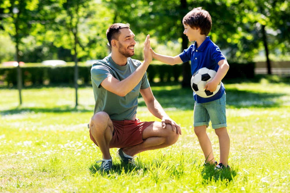 family, fatherhood and people concept - happy father and little son with soccer ball making high five gesture at summer park. father giving five to son with soccer ball at park