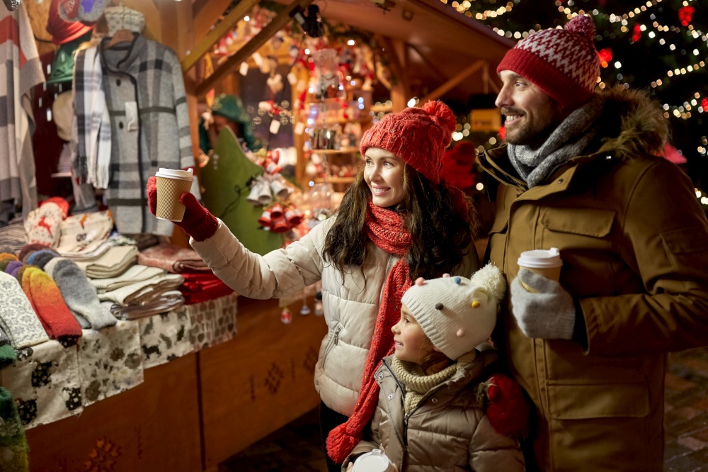 family, winter holidays and celebration concept - happy mother, father and little daughter with takeaway drinks at christmas market on town hall square in tallinn, estonia. family with takeaway drinks at christmas market