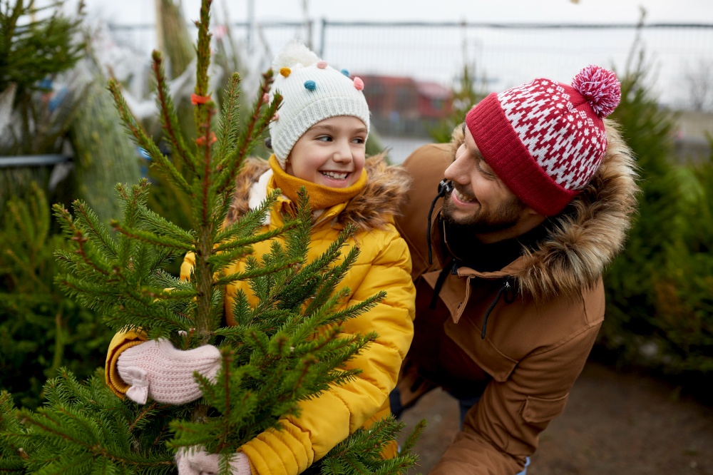 family, winter holidays and people concept - happy father and little daughter choosing christmas tree at street market. happy family choosing christmas tree at market