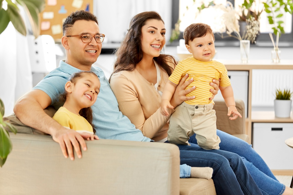 family and people concept - portrait of happy mother, father, little daughter and baby son sitting on sofa at home. portrait of happy family sitting on sofa at home