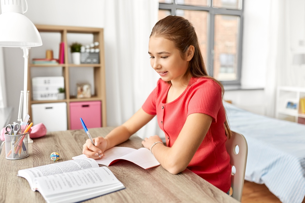 children, education and learning concept - happy smiling student teenage girl with book writing to notebook at home. student girl with book writing to notebook at home