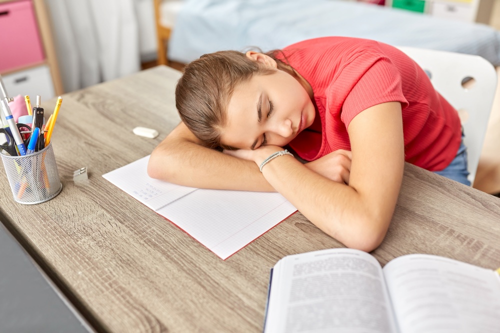 children, education and learning concept - tired teenage student girl sleeping on table at home. tired student girl sleeping on table at home
