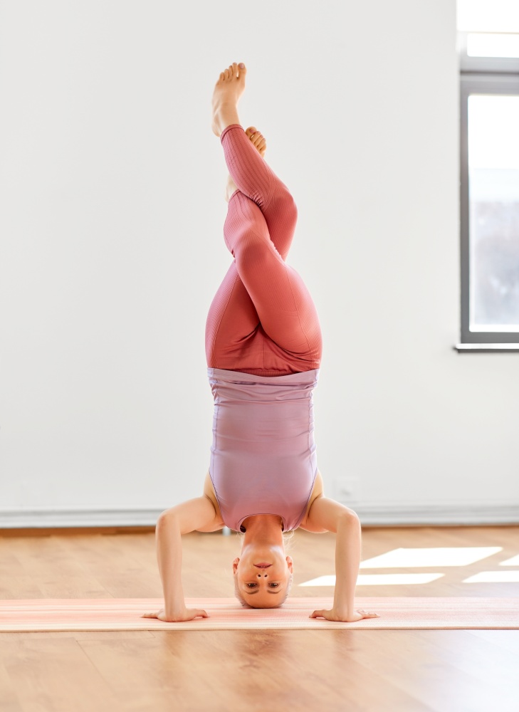 fitness, people and healthy lifestyle concept - young woman doing yoga in supported headstand at studio. woman doing supported headstand at yoga studio