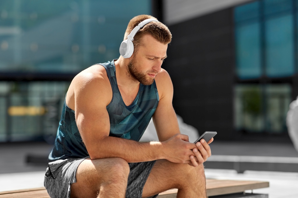 fitness, sport and technology concept - young athlete man with headphones and smartphone listening to music outdoors. young athlete man with headphones and smartphone
