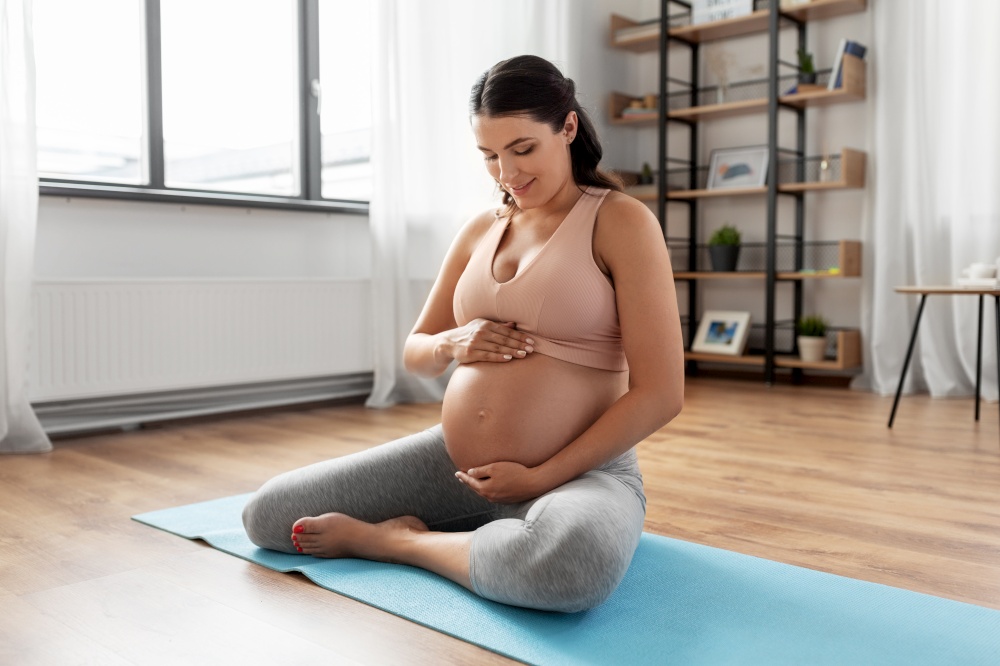 sport and people concept - happy pregnant woman sitting on yoga mat at home. happy pregnant woman sitting on yoga mat at home