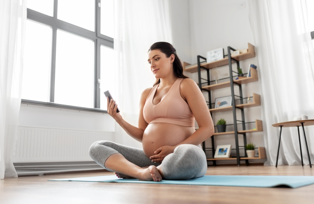 sport and people concept - happy pregnant woman with smartphone doing yoga at home. happy pregnant woman with phone doing yoga at home