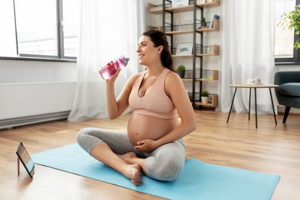 sport, fitness and people concept - happy smiling pregnant woman drinking water after yoga at home. pregnant woman drinking water after yoga at home