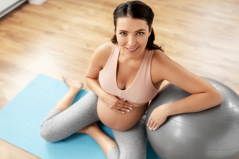 pregnancy, sport and fitness concept - happy smiling pregnant woman exercising with fitball at home. happy pregnant woman with fitball at home