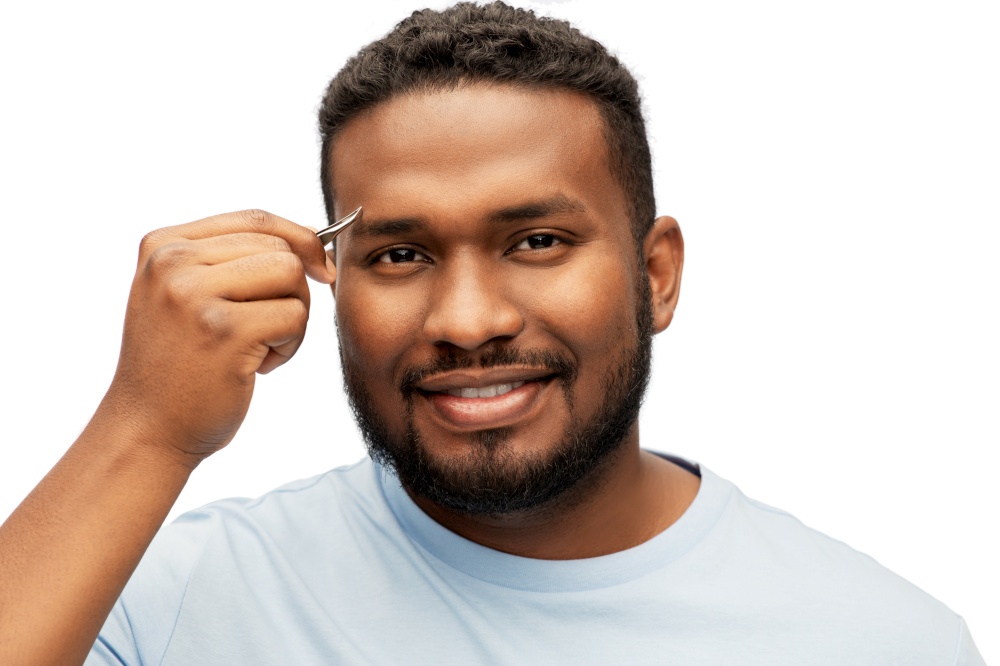grooming and people concept - smiling young african american man with tweezers tweezing his eyebrow over white background. african man with tweezers tweezing his eyebrow