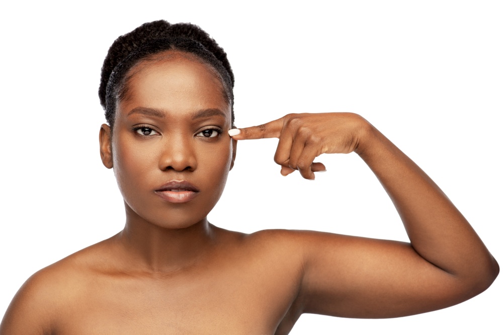 beauty and people concept - beautiful young african american woman with bare shoulders pointing to her eye over white background over white background. beautiful african woman pointing to her eye