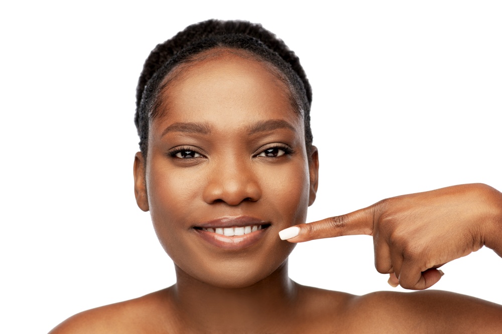 beauty, dental care and people concept - beautiful smiling young african american woman pointing to her mouth over white background. african american woman pointing to her mouth