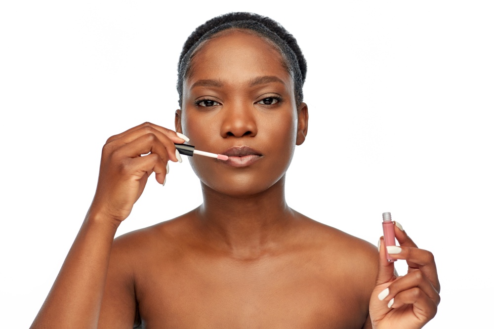 beauty, make up and cosmetics concept - beautiful young african american woman applying lip gloss over white background. african american woman applying lip gloss