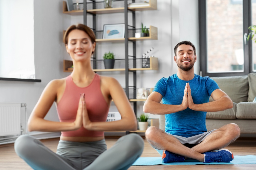 fitness, people and healthy lifestyle concept - happy smiling man and woman meditating in yoga lotus pose at home. happy couple meditating in yoga lotus pose at home