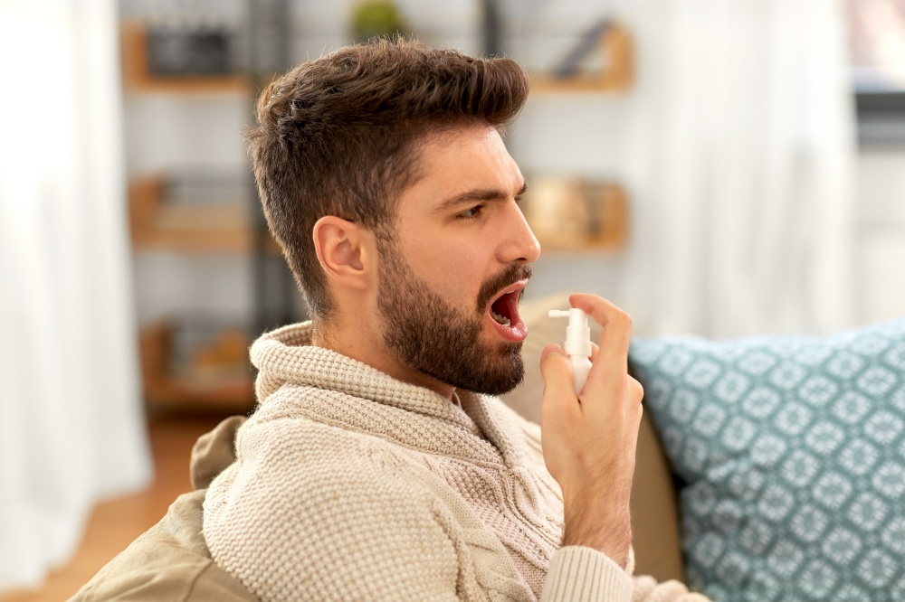 rhinitis, medicine and healthcare concept - sick indian man in blanket using oral spray at home. sick indian man using oral spray at home