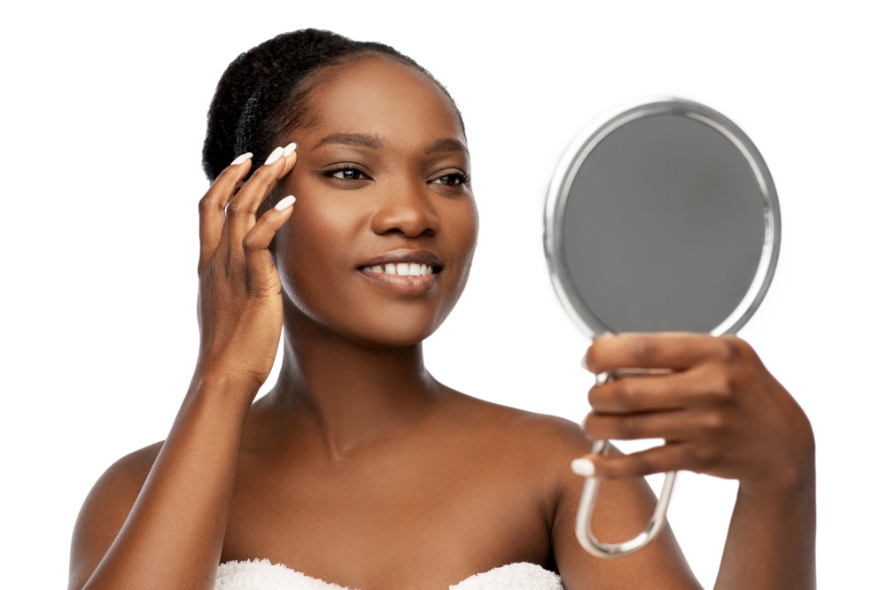 beauty and people concept - portrait of happy smiling young african american woman with bare shoulders looking to mirror over white background. smiling african american woman looking to mirror