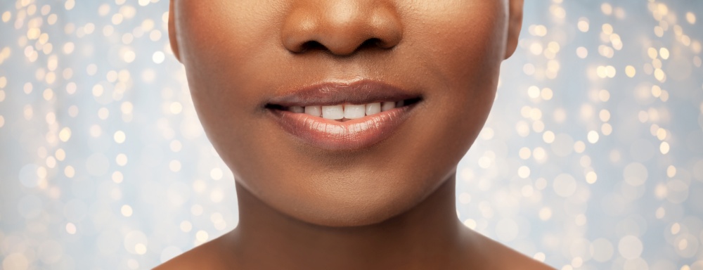 beauty, dental care and people concept - close up of face of beautiful smiling young african american woman over festive lights background. close up of face of smiling african american woman