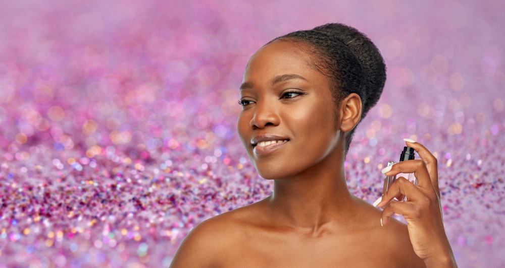 beauty, luxury and perfumery concept - portrait of happy smiling young african american woman with bare shoulders with perfume over purple glitter on background. young african american woman with perfume