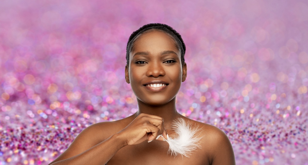 beauty, luxury and people concept - portrait of happy smiling young african american woman with bare shoulders and feather over purple glitter background. happy african american woman with feather