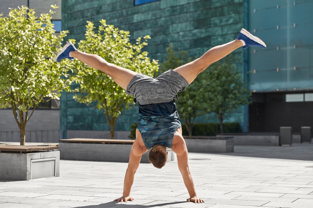 fitness, sport, training and lifestyle concept - young man exercising and doing handstand outdoors. young man exercising and doing handstand outdoors