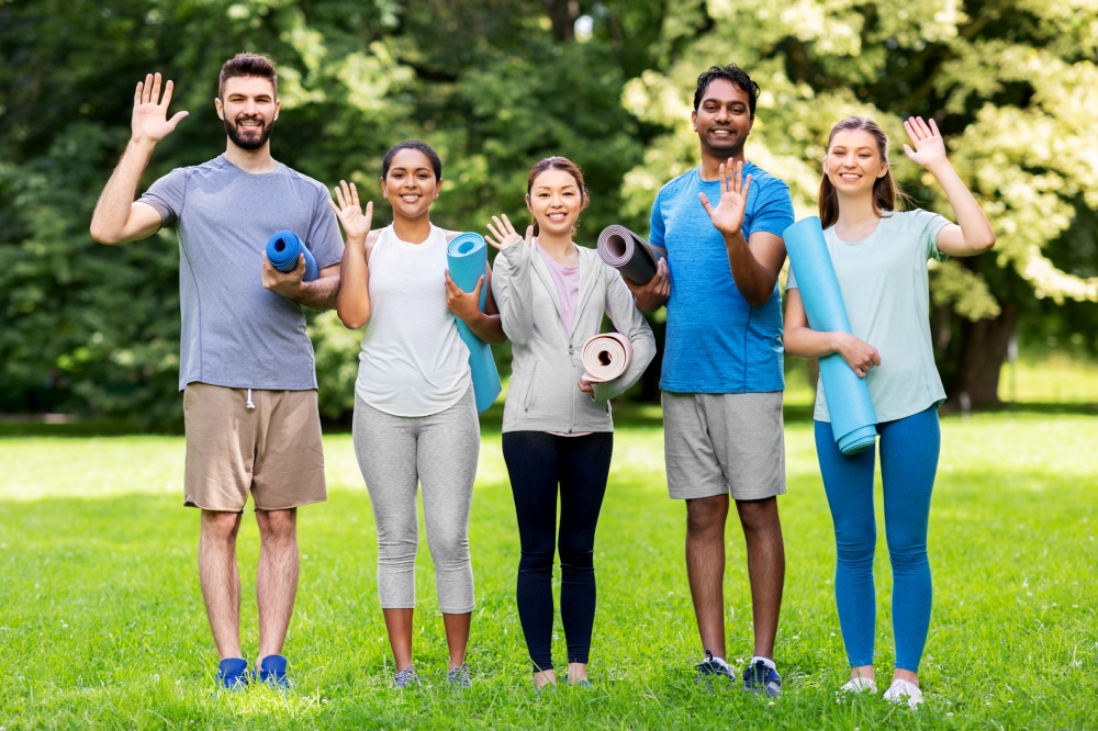 fitness, sport and healthy lifestyle concept - group of happy people with yoga mats waving hands at park. happy people with yoga mats waving hands at park
