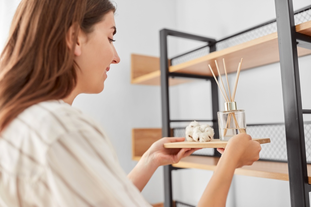 home improvement, decoration and people concept - happy smiling woman placing aroma reed diffuser to shelf. woman placing aroma reed diffuser to shelf home