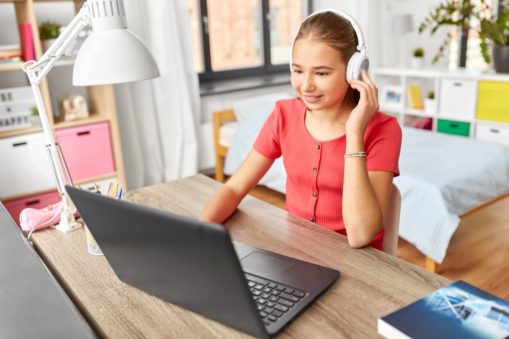 children, education and distant learning concept - happy smiling teenage student girl in headphones with laptop computer at home. girl in headphones with laptop computer at home
