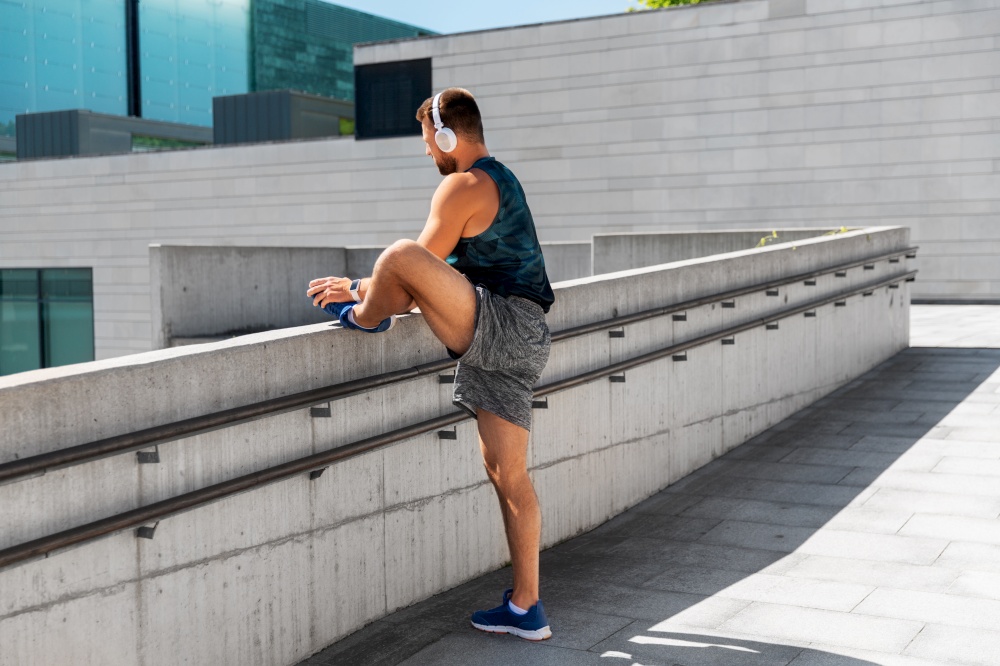 fitness, sport, training and lifestyle concept - young man in headphones stretching leg outdoors. young man in headphones stretching leg outdoors