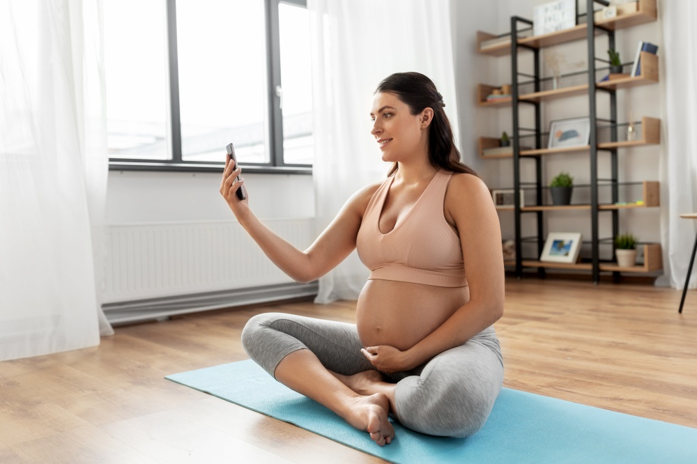 sport and people concept - happy smiling pregnant woman with smartphone exercising at home. pregnant woman with smartphone doing yoga at home