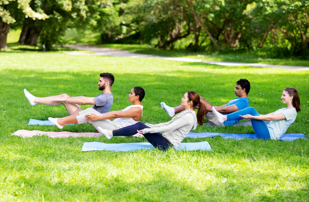fitness, sport and healthy lifestyle concept - group of happy people doing yoga at summer park. group of people doing yoga at summer park