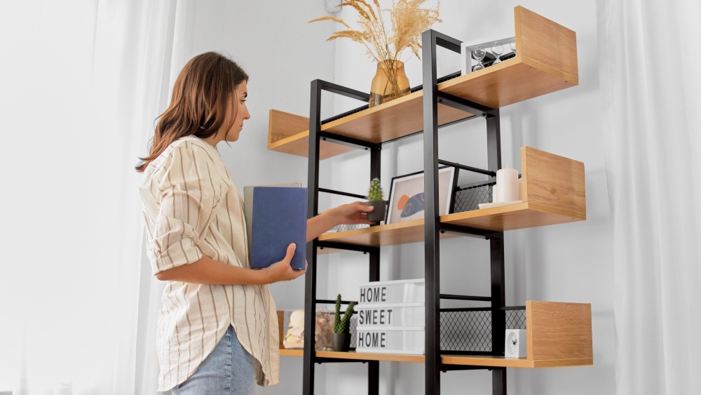 home improvement, decoration and people concept - woman arranging flower and books on shelving. woman arranging flower and books at home