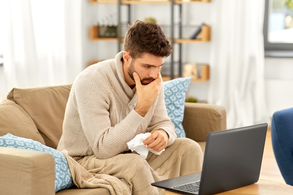 healthcare, technology and medicine concept - sick man in blanket having video call on laptop computer at home. sick man having video call on laptop at home