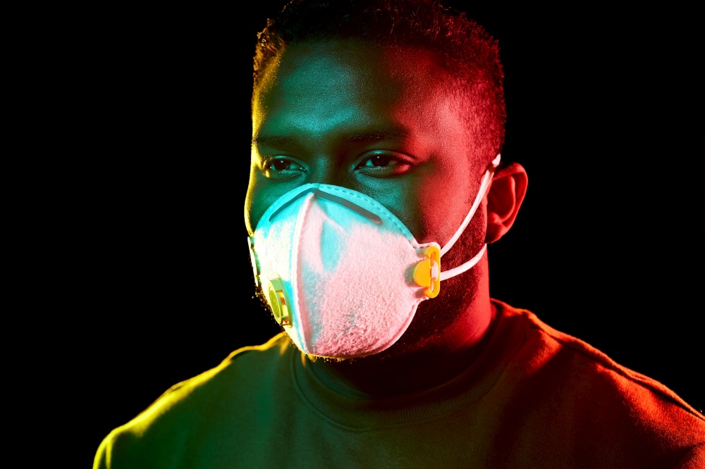 health, safety and pandemic concept - young african american man wearing protective mask or respirator over black background. african american man in mask or respirator