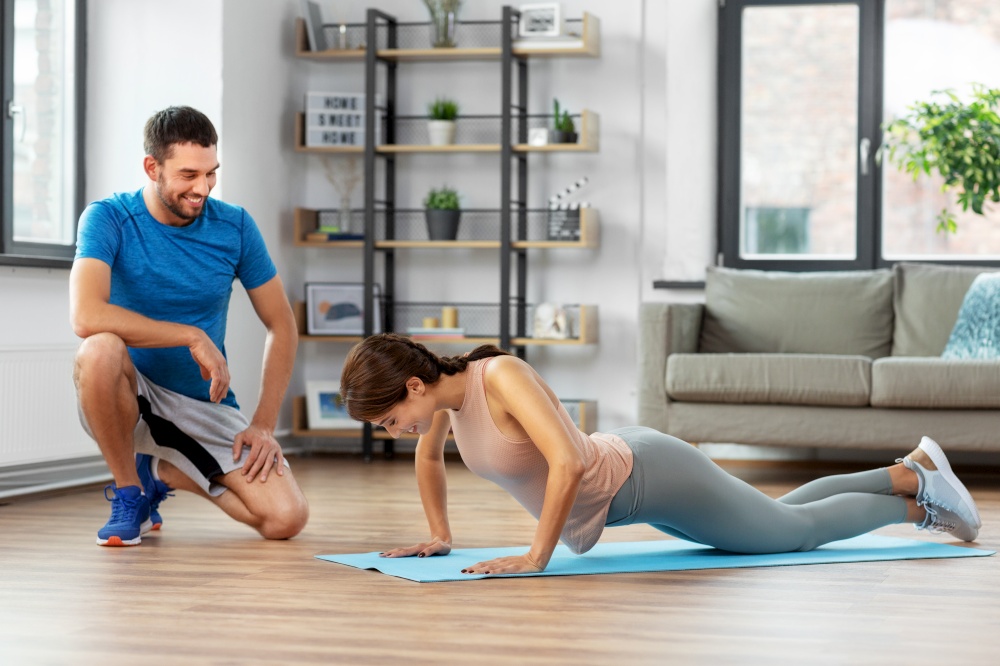 fitness, sport, training and lifestyle concept - happy smiling woman with personal trainer doing push-ups at home. woman with personal trainer doing push-ups at home