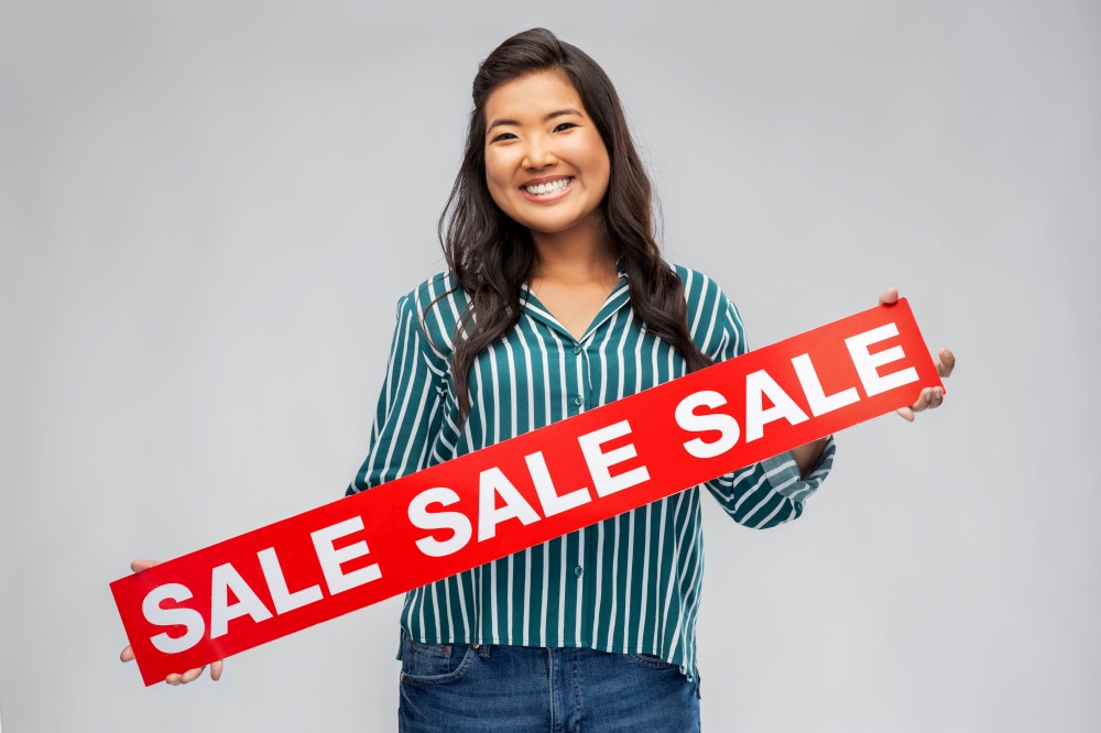 shopping and people concept - happy smiling young asian woman with sale banner over grey background. happy smiling young asian woman with sale banner