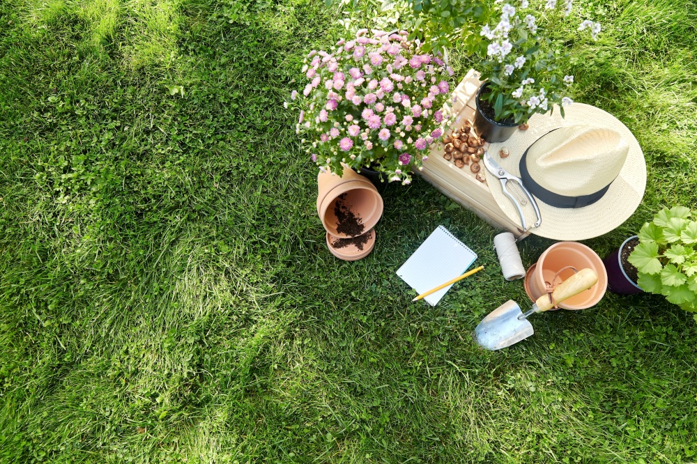 gardening and people concept - notebook with pencil, garden tools, wooden box and flowers in pots at summer. garden tools, wooden box and flowers at summer