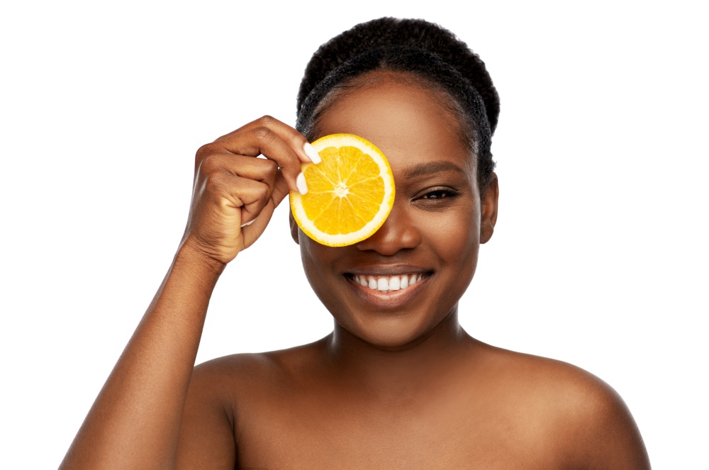 beauty, skin care and detox concept - beautiful smiling african american woman making eye mask of oranges over white background. smiling african woman making eye mask of oranges