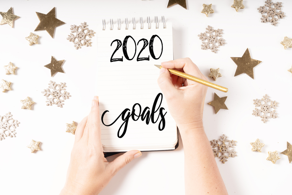 Goals for Cristmas and New 2020 Year. Holiday decorations and ruled notebook with wish list and somwones hands, flat lay top view. Christmas flat lay scene with golden decorations